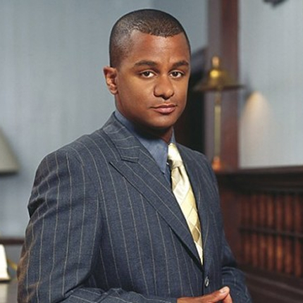 Young french black man in a gray tux looking directly at the camera