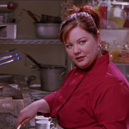 Younger white woman in a red chef jacket with her hair pulled up